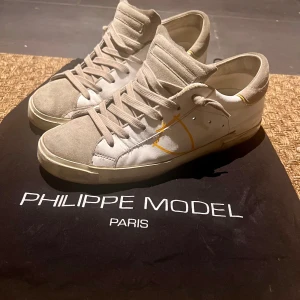 Sneakers från Philippe Model - Snygga sneakers från Philippe Model i en kombination av beige mocka och vit skinn. Skorna har en klassisk snörning och en subtil gul detalj på sidan. Perfekta för en stilren look.
