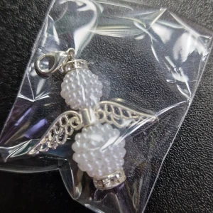 Ängelformad berlock med pärlor - Söt ängelformad berlock med vita pärlor och silverdetaljer. Perfekt att fästa på ett armband eller halsband för en personlig touch. Berlocken har vackra detaljerade vingar och en praktisk ögla för enkel fastsättning.