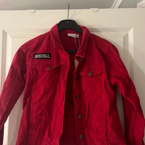 Röd jeansjacka - Snygg röd jeansjacka med ett stort tigertryck på ryggen och texten 'ORIGINAL' på framsidan. Jackan är vintage och tryck är gjort av UF företag. Aldrig använd. Säljer för 100kr + frakt eller lägg ett prisförslag 😍
