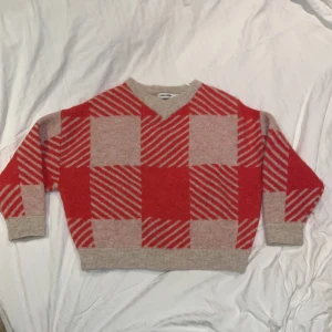 Orange och beige tröja från Carin Wester - Säljer en mysig orange och beige tröja från Carin Wester med ett rutigt mönster. Tröjan har en v-ringad hals och långa ärmar. Perfekt för att hålla sig varm under kyligare dagar. Den är använd ett fåtal gånger. 