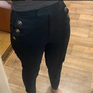 Svarta byxor med knappar - Snygga svarta byxor med hög midja och dekorativa knappar på sidorna. Perfekta för en stilren look.