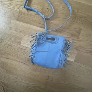 Maje väska - Snygg blå axelväska med justerbar rem och fransdetaljer på sidorna. Perfekt för att ge en bohemisk touch till din outfit. Säljer för billigt pga ingen användning längre och några små skador ( skriv priv för fler bilder) PRIS KAN DISKUTERAS 