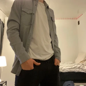 Grå överskjorta från Jack & Jones - Snygg grå skjorta från Jack & Jones med långa ärmar och knappar framtill. Skjortan har två bröstfickor med knappstängning och är perfekt för en stilren look. Pris går att diskuteras. Storlek M. 100% bomull. Använd 1-2 gånger.