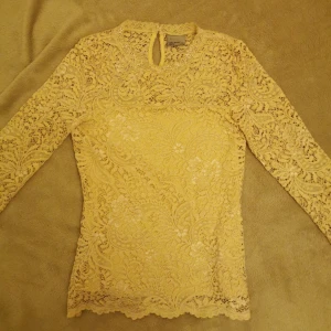 Beigel spetsblus - Säljer en elegant beige spetsblus med långärmad design. Blusen har ett vackert mönster och en liten knappdetalj i nacken. Perfekt för att lägga till en touch av stil till din garderob.