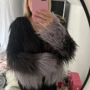 Svart och grå pälsjacka - Snygg och trendig pälsjacka i svart och grått med långa ärmar. Perfekt för att sticka ut i mängden med sin fluffiga design. Jackan har en modern look och passar bra till olika tillfällen.