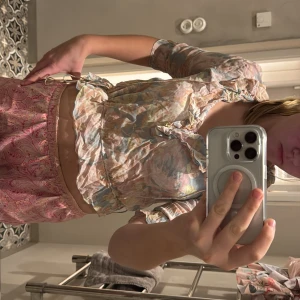 Blommig blus med volangdetaljer - Charmig blommig blus i pastellfärger med volangdetaljer och trekvartsärm. Perfekt för en somrig look. Går att dra åt där nere, har gjort det på första bilden och på andra är den lös. 