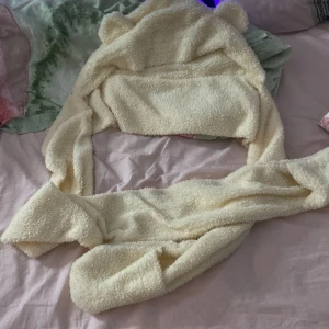 Gul fluffig mössa med öron - Söt och mysig gul mössa med små öron, perfekt för att hålla sig varm. Den är fluffig och täcker både huvud och hals, vilket gör den idealisk för kyliga dagar. Ena ”handen” är längre än den andra så att man kan ha ett varv runt halsen och sen också ha den lite hängande! Inga fler bilder