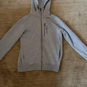 Sail Racing Hoodie - Grå hoodie från Sail Racing med dragkedja och justerbar huva. Hoodien är storlek M men passar även S. Den är nästan helt oanvänd då den är lite för stor på mig vilket även är anledningen till att den säljs. Vid frågor eller funderingar är det bara att skriva.