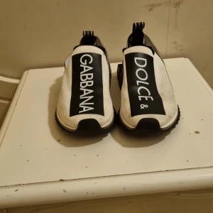 Svarta och vita sneakers från Dolce & Gabbana - Stilrena sneakers från Dolce & Gabbana i svart och vitt. Skorna har en elastisk överdel med märkets logotyp i stora bokstäver. Perfekta för en trendig look.