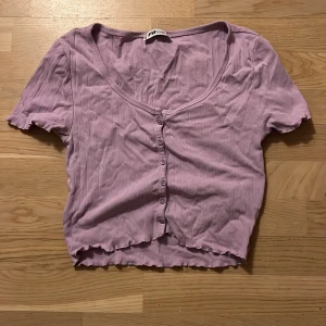 Lila ribbad topp från FB Sister - Säljer en söt lila ribbad topp från FB Sister. Toppen har korta ärmar och knappar framtill. 