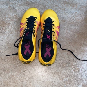 Gula fotbollsskor från Adidas - Snygga gula fotbollsskor från Adidas med svarta snören och rosa detaljer. Perfekta för fotbollsplanen med sin iögonfallande design och bekväma passform.