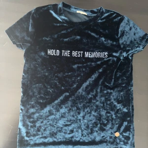  Blå sammetst-shirt med text - Snygg blå t-shirt i sammet med texten 'HOLD THE BEST MEMORIES' på framsidan. Kortärmad och mjuk, perfekt för en stilren look. PRIS KAN DISKUTERAS