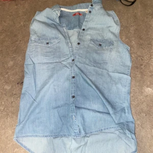 Ljusblå ärmlös jeansskjorta - Snygg ljusblå ärmlös jeansskjorta med knappar framtill och två bröstfickor. 