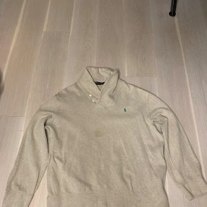 Beige tröja från Polo Ralph Lauren - Säljer en stilren beige tröja från Polo Ralph Lauren med en klassisk krage och två knappar. Den har en broderad grön logotyp på bröstet och långa ärmar. Perfekt för en avslappnad men ändå elegant look.