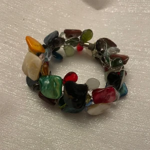 Färgglatt armband med stenar - Unikt armband med stora, färgglada stenar i olika former och färger som röd, grön, blå, gul och vit. Perfekt för att ge en färgklick till din outfit. Armbandet har en elastisk design för enkel passform.