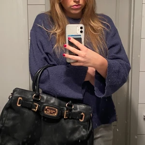 Svart skinnväska från micheal kors - Snygg svart skinnväska med eleganta rosegulddetaljer och dubbla handtag. Väskan har en stilren design med en metallplatta framtill och spännen på sidorna. Perfekt för att ge en lyxig touch till din outfit.