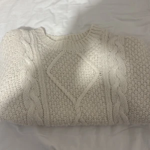 Vit stickad tröja från ASOS Design - Säljer en mysig vit stickad tröja från ASOS Design. Tröjan har ett snyggt flätmönster och ribbade kanter vid hals, ärmslut och nederkant. Perfekt för kyliga dagar!