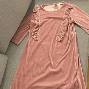 Rosa klänning från Name It - Söt rosa klänning i mjukt material från Name It. Klänningen har långa ärmar och fina volangdetaljer framtill. Perfekt för en stilfull och bekväm look.