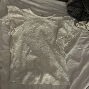 Vit blus från Holly & Whyte stolek XS - Säljer en vit blus från Holly & Whyte med ett subtilt mönster och volangdetaljer på ärmarna. Blusen har en knapp i nacken.