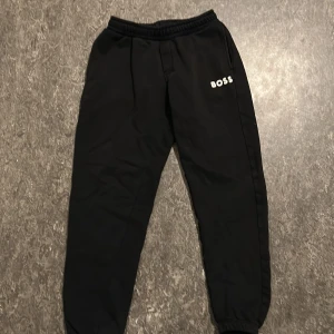 Svarta mjukisbyxor från Boss - Snygga svarta mjukisbyxor från Boss med elastisk midja och muddar vid bensluten. Perfekta för en avslappnad stil. Boss-loggan är tryckt på framsidan.