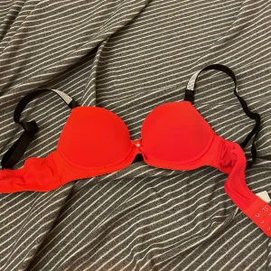 Röd bh med strassdetaljer - Snygg röd bh med glittrande strassdetaljer på axelbanden. Den har en klassisk design med justerbara band och hakknäppning bak. Perfekt för att lägga till lite glamour i vardagen.