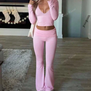 Rosa omlottopp och byxor - Snyggt set med en rosa omlottopp och matchande byxor. Toppen har en v-ringad design och långa ärmar, medan byxorna har en utsvängd passform. Perfekt för en stilren och bekväm look.” Tryck inte på köp nu