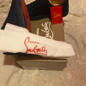 Mörkblå sneakers från Christian Louboutin - Snygga mörkblå sneakers från Christian Louboutin i mocka. Skorna har en klassisk design med snörning och den ikoniska röda sulan. Perfekta för en stilren look. pris kan diskuteras!!!