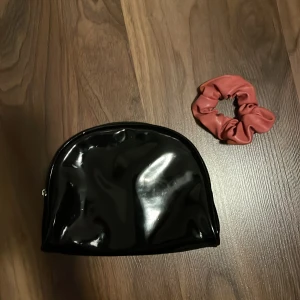 Svart necessär och rosa scrunchie  - Säljer en svart glansig necessär och en scrunchie. Båda är i bra skick necessären har några små repor som bara syns om man kollar nära. Priset gäller för båda tillsammans! ⭐️ 