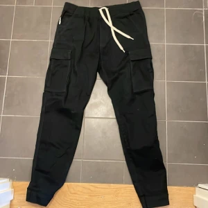 Svarta cargobyxor från Yoke - Snygga svarta cargobyxor från Yoke med praktiska fickor på sidorna och en bekväm snörning i midjan. Perfekta för en avslappnad stil.