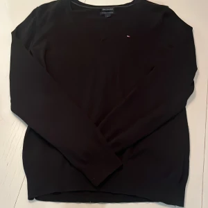 Svart tröja från Tommy Hilfiger - Säljer en svart tröja från Tommy Hilfiger. Med V-ringning. Tröjan har en liten logga på bröstet och ribbstickade kanter vid hals, ärmslut och nederkant. Storleken passar som S. Perfekt för både vardag och lite finare tillfällen. 🤍