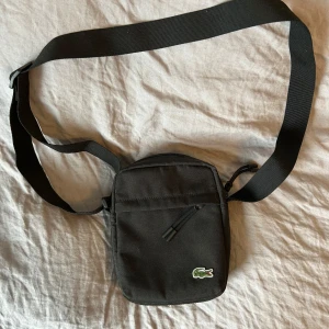 Lacoste väska - En väska av märket Lacoste som köptes i Frankrike för något år sedan och har inte använts alls. Jag kan ha haft på mig den någon enstaka gång men den är i helt nyskick. Priset var någonstans kring 1000 då. Pris kan diskuteras vid snabb affär