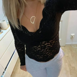 Svart spetsblus - Snygg svart spetsblus med långärmad design och v-ringad hals. Perfekt för en stilren look med en touch av elegans. Blusen är figurnära och har ett genombrutet mönster som ger en trendig känsla.
