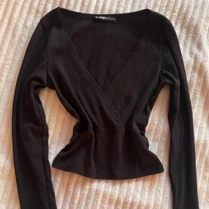 Svart ribbad topp från NewYorker - Snygg svart ribbad topp från  NewYorker med v-ringning och långa ärmar. Lite stor vid v-ringningen rekommenderar ett linne under, bra för layering av kläder! 