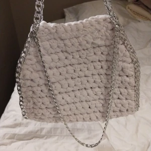 Vit virkad väska med kedjedetaljer - Snygg vit virkad väska med silverfärgade kedjedetaljer. Perfekt för att ge din outfit en unik touch. Väskan har en mjuk och mysig känsla med ett modernt utseende.