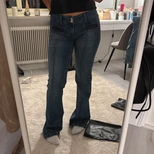 Blå bootcut jeans - Snygga blå bootcut jeans med låg midja och dekorativa sömmar. Perfekta för en avslappnad stil med en touch av retro. De har fickor fram och bak samt en knapp- och dragkedjestängning.