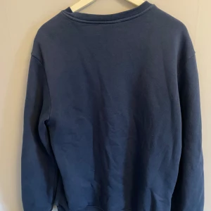 Blå sweatshirt från H&M - Säljer en blå crewneck sweatshirt från H&M i relaxed fit. Tröjan har långa ärmar och ribbade muddar vid ärmslut och nederkant. Perfekt för en avslappnad stil. Köpt från herravdelningen men passar för båda!