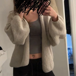 Kofta Lindex - Mysig grå/beige kofta som är långärmad. Perfekt för att hålla sig varm under kyligare dagar. Koftan har en lös passform och är tillverkad i ett mjukt material.