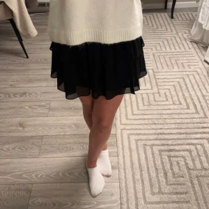 Svart kjol från Chelsea - Snygg svart kjol från Chelsea med volangdetaljer och elastisk midja. Perfekt för en stilren look. Helt oanvänd och i nyskick