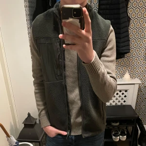 Oliv grön fleeceväst med dragkedja - Säljer en oliv grön fleeceväst med dragkedja. Västen har en praktisk design med fickor och är perfekt för lager-på-lager under kyligare dagar. Skick 10/10 aldrig använd 