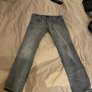Grå slim fit jeans - Snygga grå slim fit jeans från Jack & Jones, modell Glenn. Perfekta för en stilren look med klassisk femficksdesign och knappgylf. Passar utmärkt till både vardag och mer uppklädda tillfällen.