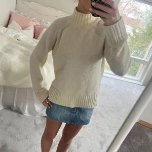 Vit stickad polotröja - Mysig vit stickad polotröja med ribbade muddar och hög krage. Perfekt för kyliga dagar och ger en stilren look. Passar bra till både jeans och kjol.