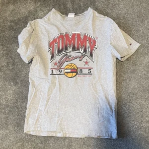 Grå t-shirt från Tommy Jeans - Snygg grå vintage t-shirt från Tommy Jeans med ett stort tryck på framsidan. Använts en del men inga tydliga defekter. 