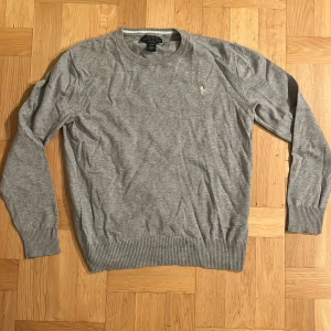 Grå tröja från Ralph Lauren - Säljer en stilren grå tröja från Ralph Lauren med rund halsringning och broderad logotyp på bröstet. Har använts en del men har mycket liv kvar!