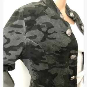 Camouflage kavaj med knappar - Snygg kavaj i camouflage-mönster med dekorativa knappar framtill. Jackan har en modern look med uppvikta ärmar och en bekväm passform. Perfekt för att ge din outfit en cool touch.i ny skick