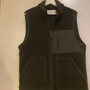 Grön fleeceväst från A Day's March - Säljer en grön fleeceväst från A Day's March storlek Medium.  Västen har en dragkedja framtill och en bröstficka med dragkedja. Perfekt för lager-på-lager under kyliga dagar. Knappt Använd. 