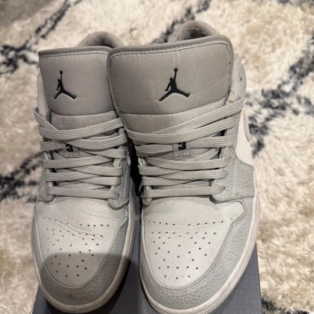 Snygga grå Nike Air Jordans med klassisk design och snörning. Skorna har en stilren look med den ikoniska Jumpman-loggan på plösen. Perfekta för dig som älskar sneakers med en tidlös stil.. Kengät.