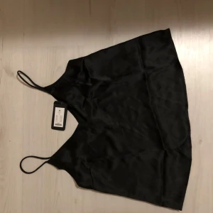 Svart satinlinne - Snyggt svart linne i satin med tunna axelband. Perfekt för en stilren look. Ny med prislapp.