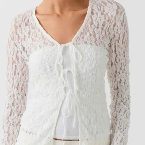 Vit spetskofta från Gina Tricot -  vit spetskofta från Gina Tricot. Koftan har långa ärmar och knytning framtill, perfekt för att lägga till en romantisk touch till din outfit. Passar bra till både vardag och speciella tillfällen.  Använd endast två gånger så den är nästan som ny! Även helt SLUTSÅLD