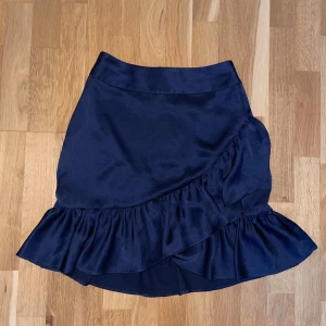 Mörkblå kjol från Holly & Whyte - Snygg mörkblå kjol från Holly & Whyte med volangdetaljer och dragkedja bak. Strl Xs och har endast använt den en gång.