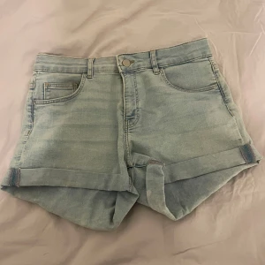 Ljusblå jeansshorts från H&M - Snygga ljusblå jeansshorts från H&M med upprullade ben och klassisk femficksdesign. Perfekta för varma sommardagar. De har en knapp och dragkedja framtill för enkel på- och avtagning.